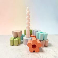 Load image into Gallery viewer, A pastel-colored candle set on a light gray surface against a soft gradient background. The set includes a tall, twisted white candle in the center, surrounded by flower-shaped and cylindrical candle holders in peach, orange, mint green, light green, light blue, lavender, and gray.
