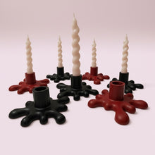 Load image into Gallery viewer, A set of spiral taper candles displayed in black and red snowflake-shaped holders on a soft pink background.
