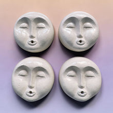 Load image into Gallery viewer, Four round white ceramic face ornaments with closed eyes and small holes in the mouths, arranged in a 2x2 grid on a pastel gradient background.
